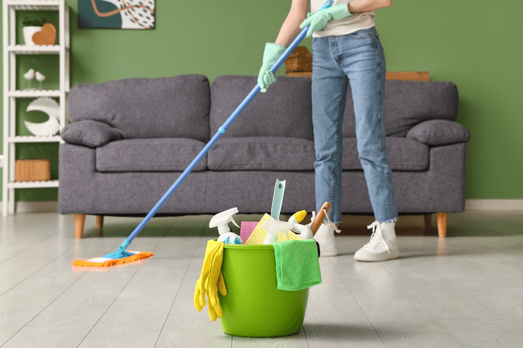 Cleaner mopping a living room floor with a bucket of supplies in the foreground